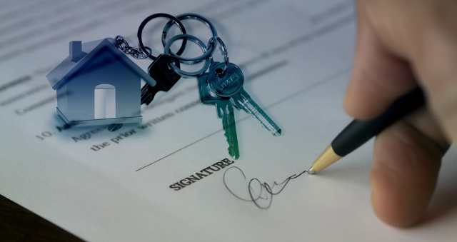 A picture of a person signing a contract with a keys and a keyring of a house in the background