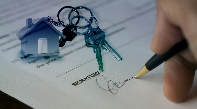 A picture of a person signing a contract with a keys and a keyring of a house in the background