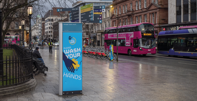 An image of the centre of Belfast with buses whizzing past COVID-19 signs