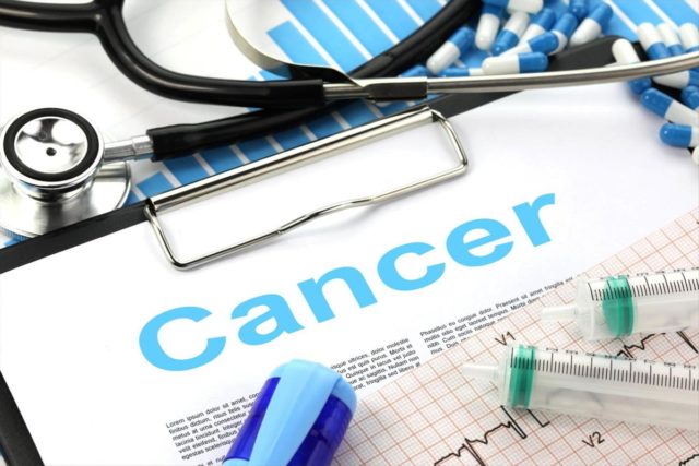 An image of a clipboard with the word 'cancer' on it, surrounded by items of medical equipment