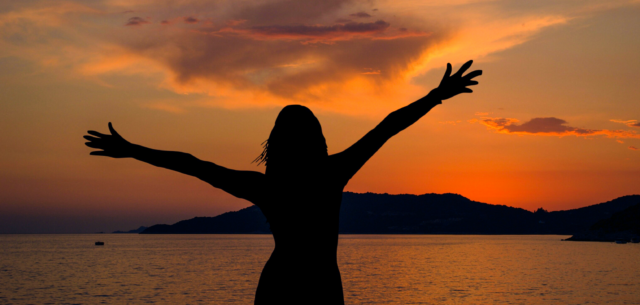 A stock image showing a silhouette of a person with their arms raised and a sunset behind