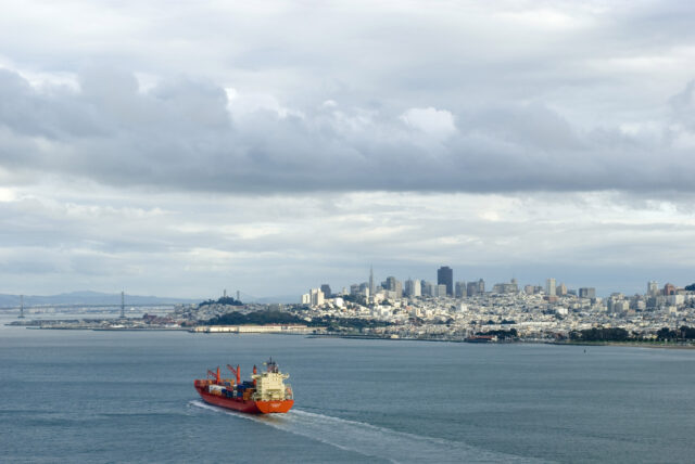 A large vessel carrying shipping containers moving towards a port city
