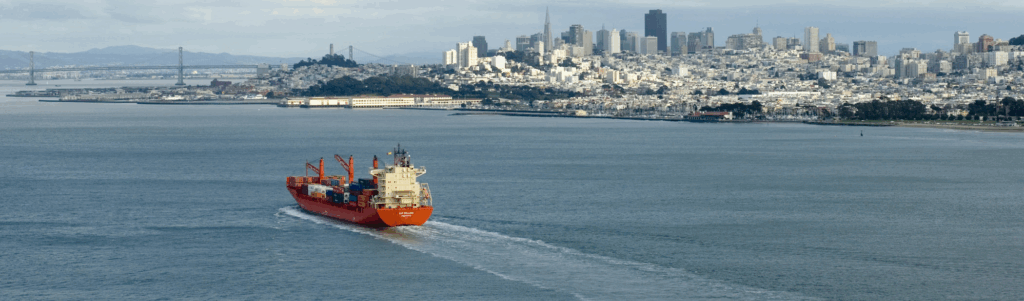 A large vessel carrying shipping containers moving towards a port city
