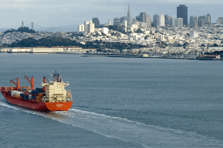 A large vessel carrying shipping containers moving towards a port city