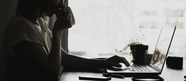A black and white image showing a woman using a laptop.