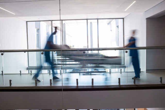 Two health and social care workers pushing a medical trolley along a hospital corridor (image: Freepik)