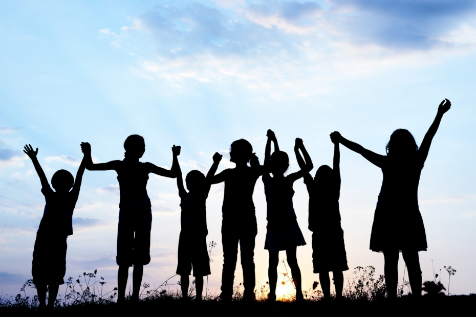 A photograph showing a silhouette of some children with a sunset behind. The children are holding hands.