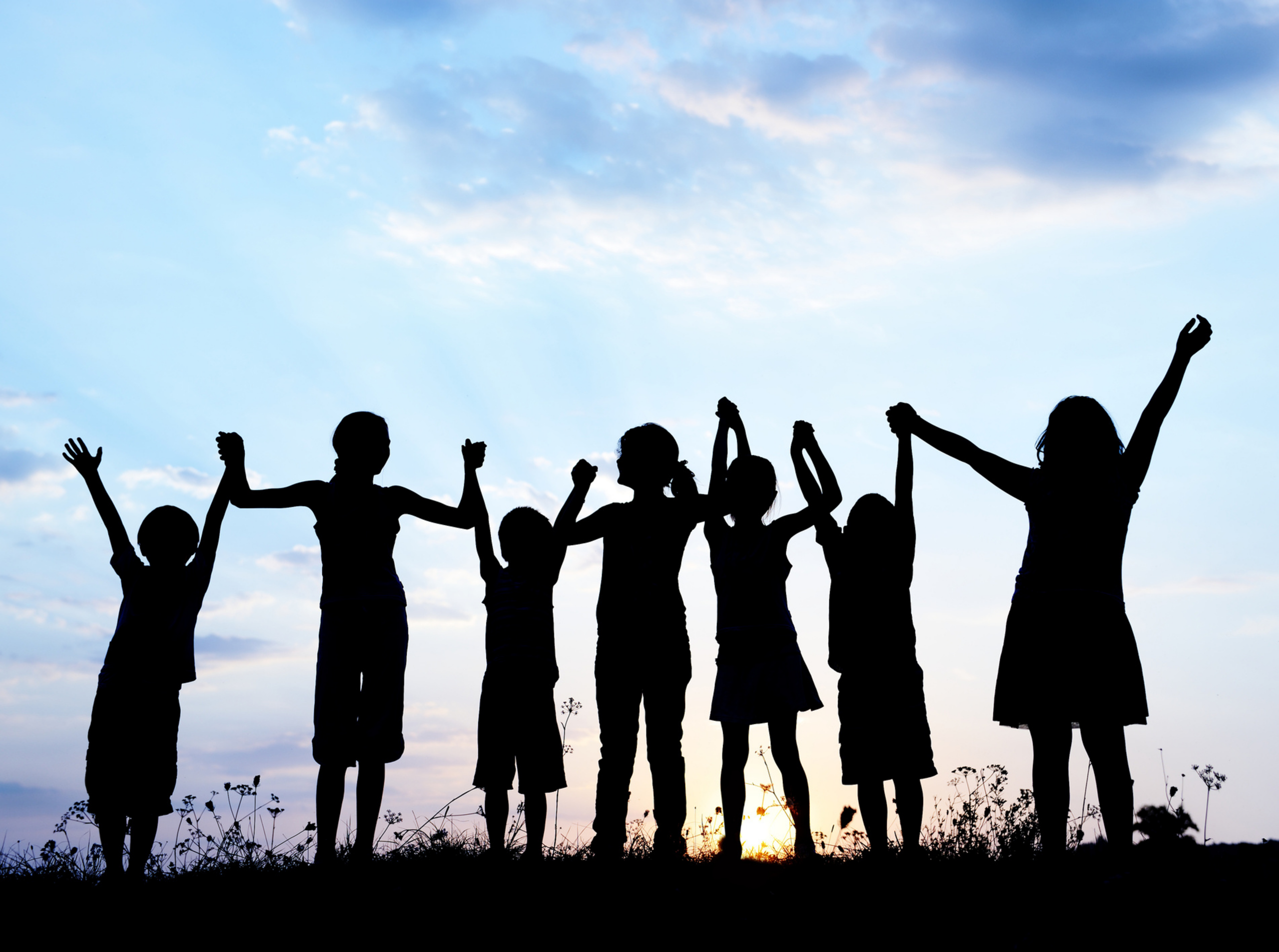 A photograph showing a silhouette of some children with a sunset behind. The children are holding hands.