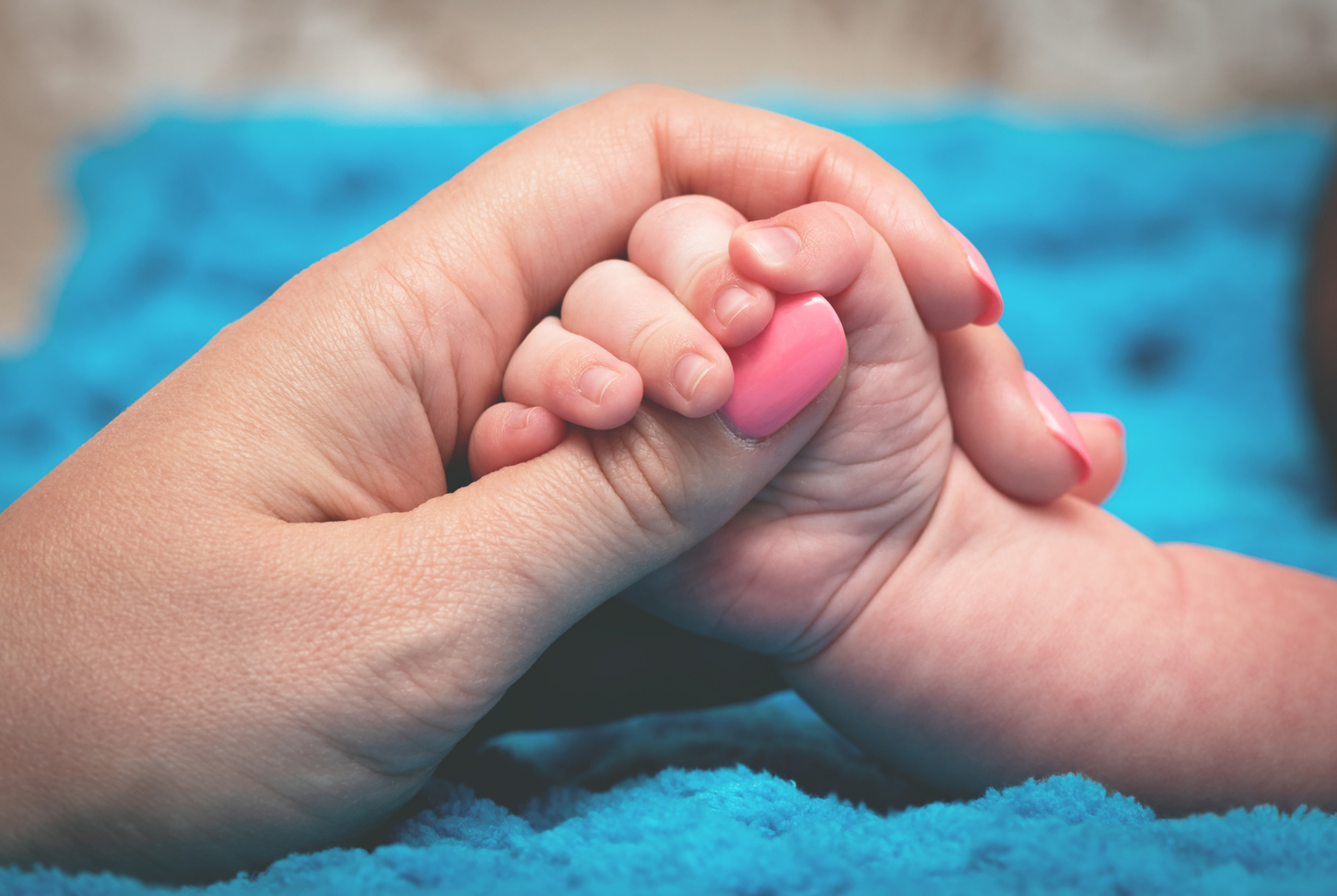 An image showing a baby's hand clutching an adult's hand.